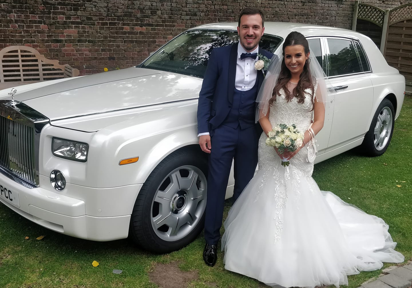 Newly weds standing infront of a Phantom wedding car